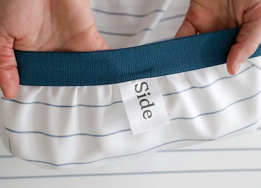 Close-up of the Ocean Stripe fitted sheet showing a sewn-in tab on the side, designed to help identify the sheet’s orientation for easy bed making.